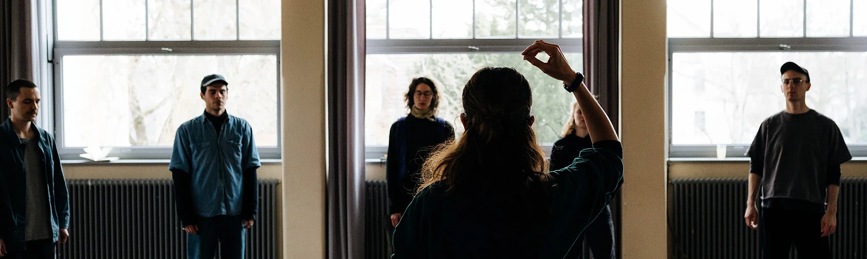 Participants in a workshop for the »In-Tune« project stand in a bright room. A person in the foreground raises their arm.