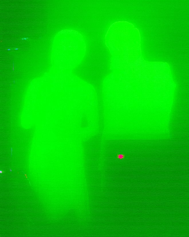 Two people appear as bright silhouettes against a luminous green screen.