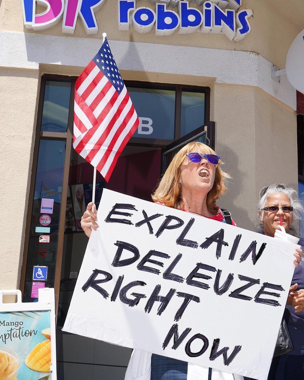 Person holding a sign: “Explain Deleuze right now“.